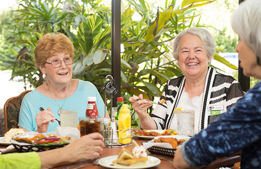 Three senior women laughing and talking at lunch.