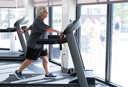 Senior woman walking on a treadmill in the John Knox Village gym.