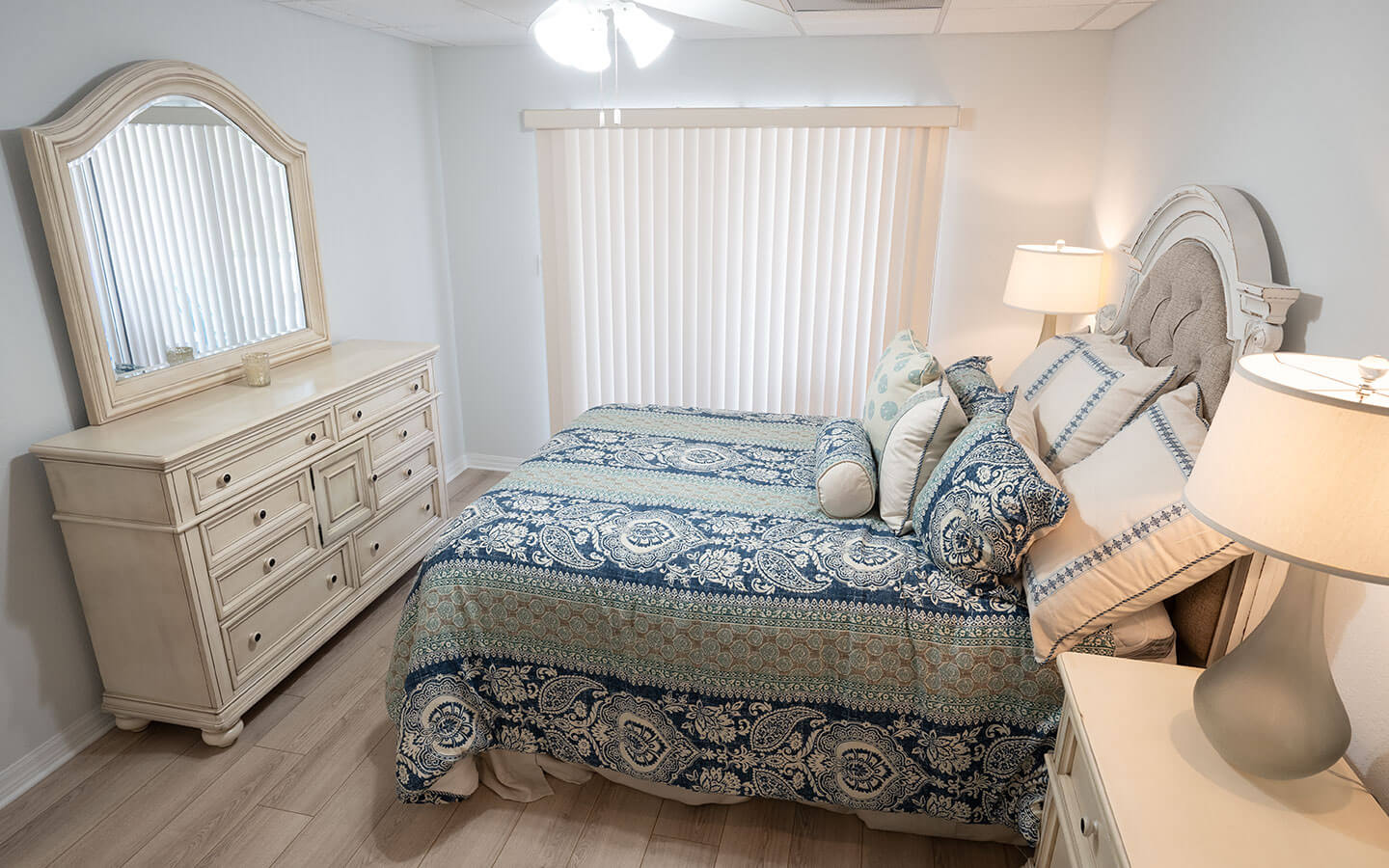 Senior living apartment bedroom with large bed, dresser and two side tables with lamps.