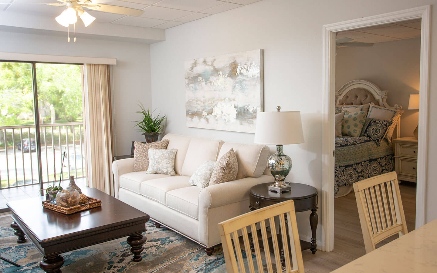 View of living room wit tan couch and door to primary bedroom with large bed.