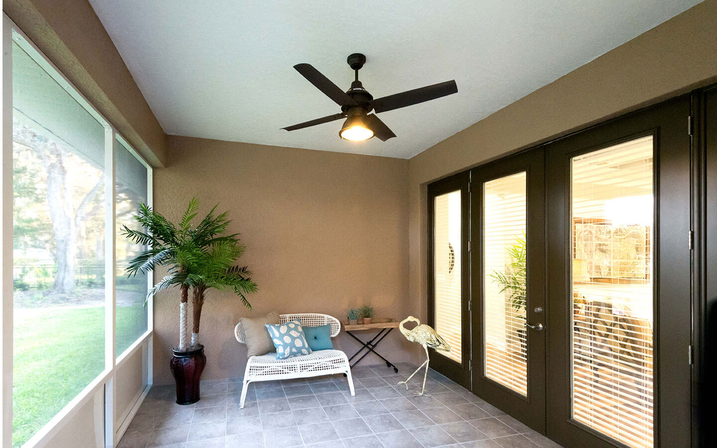 Screened in patio with ceiling fan and small bench for seating.
