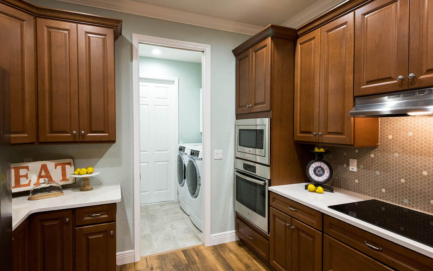 Large kitchen with dark wood cabinets, stove, oven and microwave with a view into the laundry room.